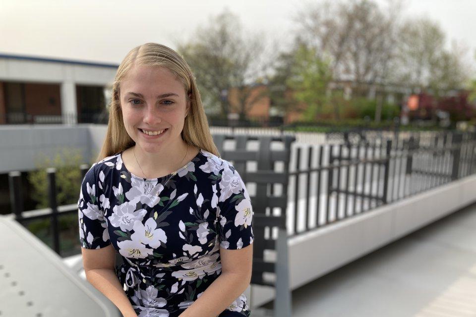 Isabelle LaBelle '23, in floral dress, sits at a table in the courtyard outside the library.